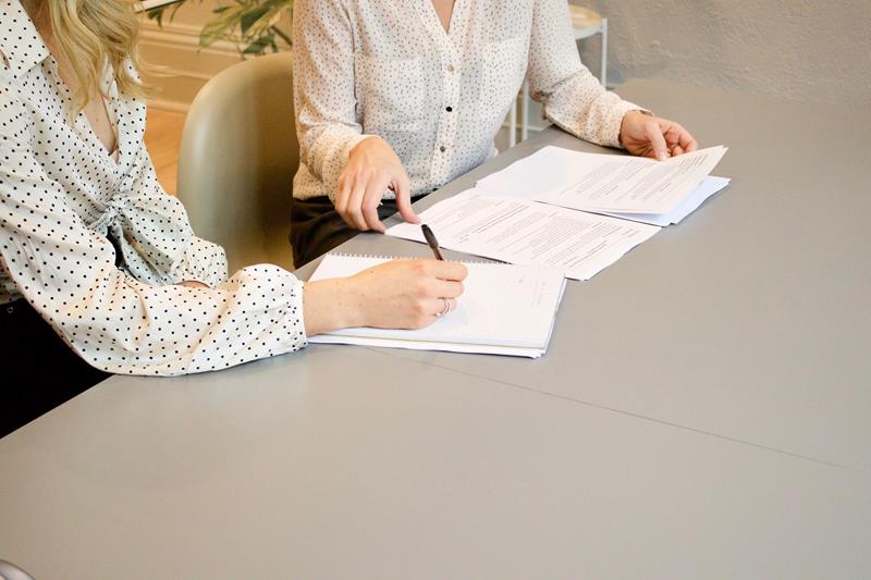 Mãos de duas mulheres em mesa de escritório, assinando papeis e representando a escritura de um inventário.